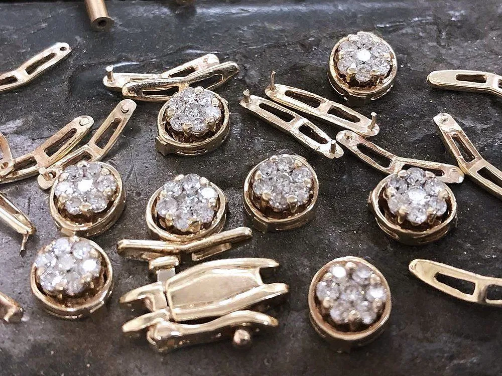 Diamond cluster earring components on Charlie Goss's jeweler's bench, mid-build